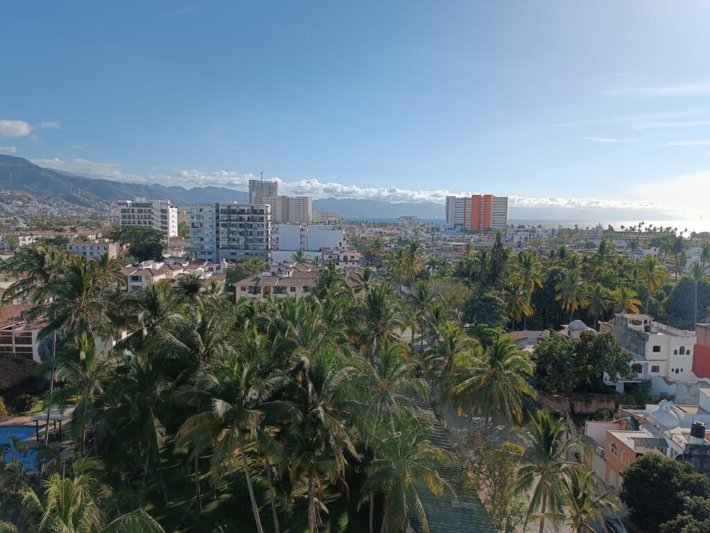 View of Versalles Puerto Vallarta with tropical palm trees, modern condominiums, mountains, and Banderas Bay in the background