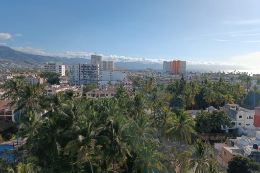 View of Versalles Puerto Vallarta with tropical palm trees, modern condominiums, mountains, and Banderas Bay in the background
