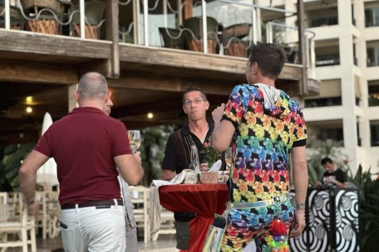 “Group of people socializing at an outdoor real estate networking event with drinks and conversation”