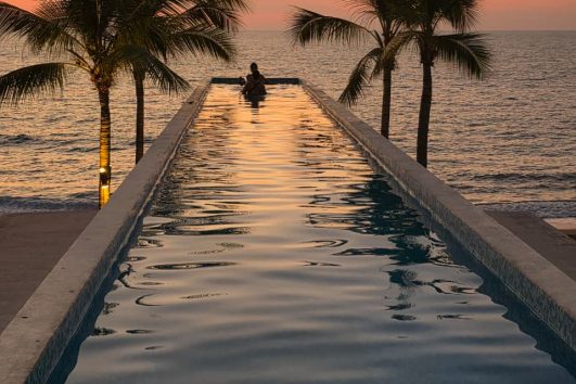 Infinity pool at sunset overlooking the ocean in Puerto Vallarta with palm trees