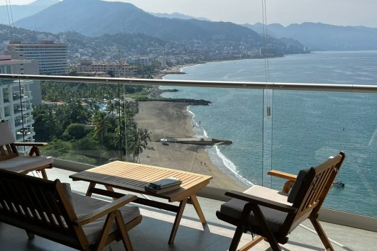 Ocean view from a luxury penthouse balcony with wooden outdoor seating in Puerto Vallarta